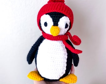 May include: A crocheted penguin wearing a red hat and scarf. The penguin is white with a black head and wings. The penguin has a yellow beak and feet.