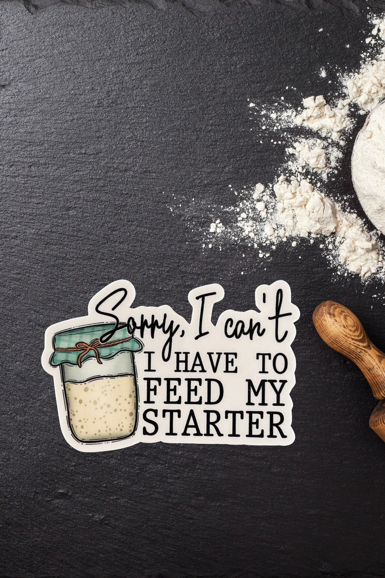 May include: A sticker with the text "Sorry, I can't, I have to feed my starter" next to a jar illustration. The jar has a green lid and a brown string tied around it. Flour and a rolling pin are in the background.