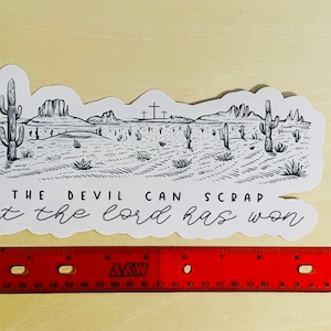May include: Black and white illustration of a desert landscape with cacti and crosses. The text "THE DEVIL CAN SCRAP but the lord has won" is written below the image.