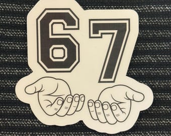 May include: A white sticker featuring the number "67" in a bold, black, collegiate-style font. Below the numbers are two stylized hands, palms up. The sticker is on a dark, textured background.