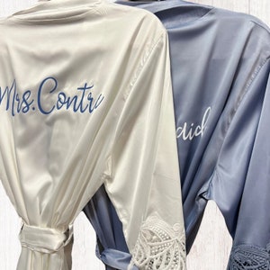 May include: Two satin robes with lace trim. One robe is white with blue embroidery that says "Mrs. Contrera". The other robe is blue with white embroidery that says "Maid of Honor".