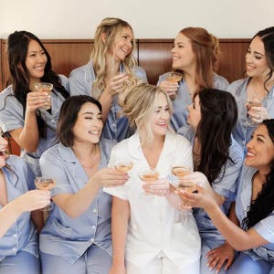 May include: A group of women wearing matching light blue pajamas raise their champagne glasses in a toast. They are smiling and looking at each other. One woman is wearing a white robe.