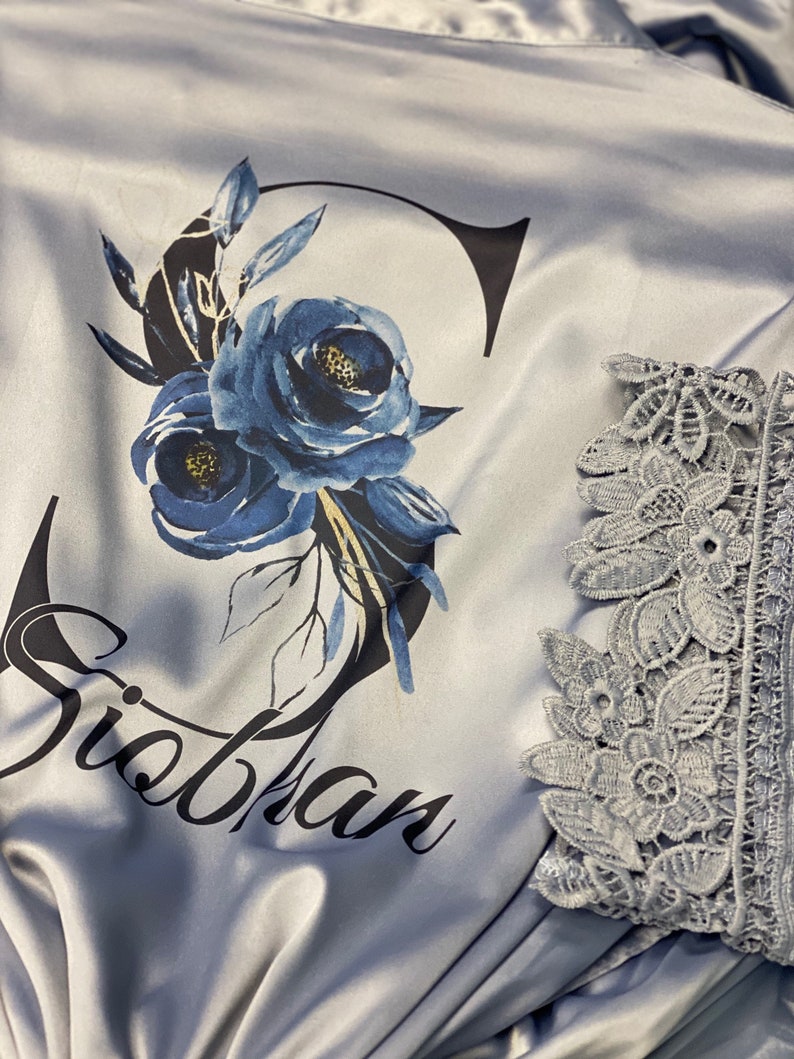 May include: A light blue satin robe with a floral design and the name "Siobhan" printed on the front. The robe has lace trim on the sleeves.