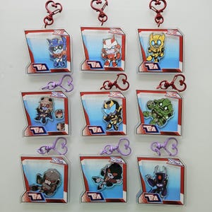May include: Nine clear plastic keychains featuring colourful cartoon characters. Each keychain has a heart-shaped loop at the top and the text 'TFA' at the bottom. The characters are from the Transformers franchise.