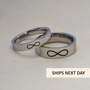 May include: Two silver rings with an infinity symbol engraved on each. The rings are stacked on top of each other.