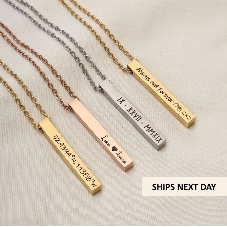 Four vertical bar necklaces in different colors and engravings laid on a light gray surface