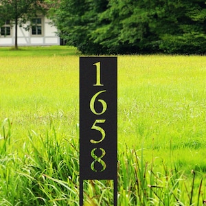 Peut inclure: Un panneau de numéro de maison en métal noir avec les chiffres 1658 découpés. Le panneau est debout dans un champ herbeux.
