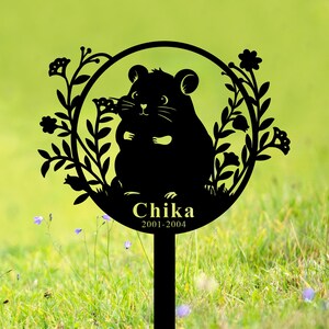 Könnte beinhalten: Schwarzer Garten-Gedenkstein aus Metall mit einer Silhouette eines Hamsters, Blumen und dem Text "Chika 2001-2004".