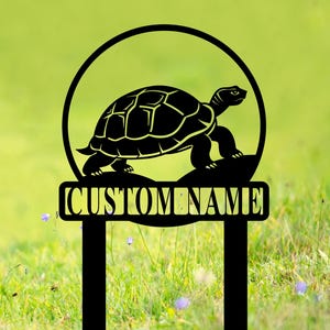 Puede incluir: Estaca de jardín de metal negro con una silueta de una tortuga caminando en círculo. La estaca tiene un letrero rectangular que dice "CUSTOM NAME".