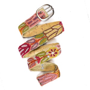 May include: A colorful embroidered belt with a silver buckle. The belt is made of a beige fabric and features a variety of floral designs in shades of pink, red, green, and yellow.