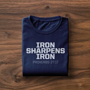 以下が含まれることがあります： 「IRON SHARPENS IRON」と「PROVERBS 27:17」という白い文字が書かれたネイビーブルーのTシャツです。