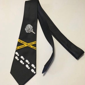 May include: Black tie with a crime scene theme. Features a white fingerprint with a magnifying glass, yellow caution tape with "DO NOT CROSS CRIME SCENE" text, and white footprints. A unique accessory for law enforcement or crime enthusiasts.