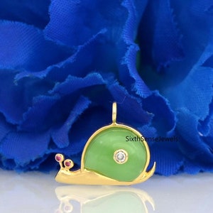 May include: A gold snail charm with a green enamel shell and a clear diamond in the center. The snail has two small pink enamel dots on its head.