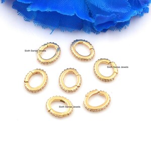 Puede incluir: Seis anillos de salto ovalados de color dorado con una fila de piedras brillantes transparentes alrededor del borde. Los anillos están abiertos y tienen un cierre con bisagra. "Sixth Sense Jewels" está impreso en el fondo blanco.