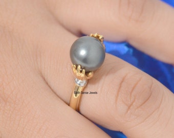 May include: A gold ring featuring a black pearl set in a gold claw setting. The ring is worn on a finger.