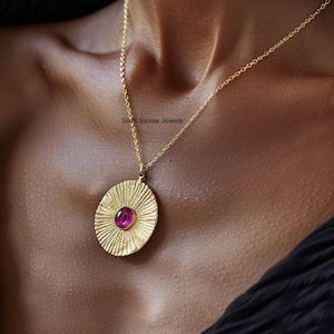 Puede incluir: Un collar de oro con un colgante redondo que presenta una piedra preciosa rosa rodeada de rayos dorados texturizados. El colgante está unido a una cadena de oro delicada. El texto "Sixth Sense Jewels" es visible en la imagen.