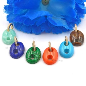 Op de afbeelding: Een verzameling kleurrijke edelsteenhangers met gouden oorringen. Elke hanger heeft een unieke kleur, waaronder blauw, groen, oranje en bruin. De ovale hangers hebben een cirkelvormige uitsparing.