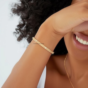 May include: A gold-colored bracelet with a textured surface and small, round, clear stones. The bracelet is worn on a person's arm. The text "Sixthsense jewels" is visible on the bracelet.