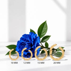 May include: Four gold-toned hoop earrings arranged in a row, labeled 10 MM, 12 MM, 15 MM, and 20 MM, positioned in front of a vibrant blue carnation flower with green leaves. The text Sixth Sense Jewels is visible in the center of the image.
