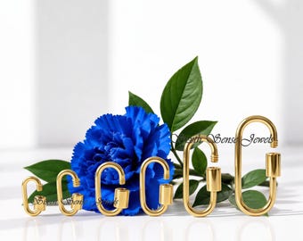 May include: A set of six gold-toned metal oval carabiner clasps arranged in increasing size order. Each clasp features a threaded screw-gate mechanism for opening and closing. The carabiners are positioned in front of a vibrant blue carnation flower.