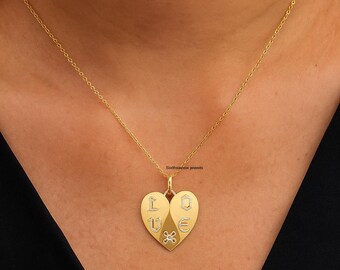 Puede incluir: Un collar con colgante en forma de corazón dorado. El colgante muestra la palabra "LOVE" con detalles de diamantes. La cadena es fina. El collar lo lleva una persona.