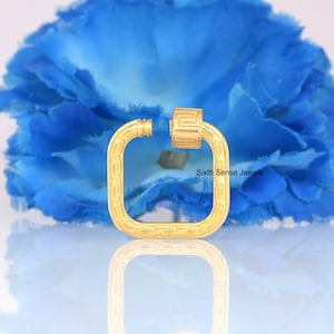 May include: A gold-colored, square-shaped jewelry clasp with a decorative pattern. The clasp is open, revealing the screw mechanism. The background features a large, blue flower and the text "Sixth Sense Jewels".