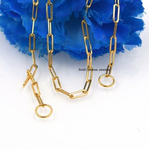 Puede incluir: Un collar de cadena de oro con un diseño de cadena de eslabones cuadrados. La cadena tiene un cierre de langosta y un anillo de salto.