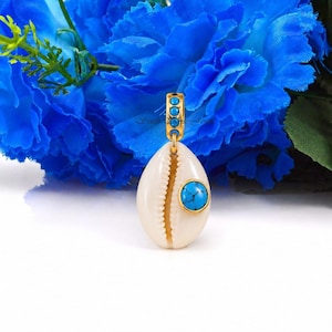 Peut inclure: Pendentif doré avec un coquillage crème et une pierre turquoise. Le pendentif présente des détails dorés et une bélière dorée avec trois petites pierres turquoises. Le fond présente des fleurs bleues.