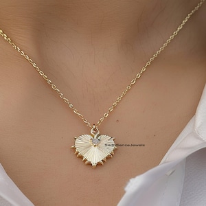 Op de afbeelding: Een gouden ketting met een hartvormige hanger. De hanger heeft een getextureerd oppervlak en een kleine, heldere steen in het midden. De tekst "SellSenceJewels" is zichtbaar in de rechterbenedenhoek van de afbeelding.