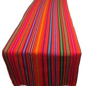 May include: A vibrant, striped table runner in shades of red, orange, pink, purple, green, and blue. The runner features vertical stripes and a white tassel trim along the bottom edge. This textile is suitable for home decor.