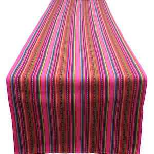 May include: A pink table runner with colorful stripes and a geometric pattern. The runner is made of woven fabric and has a fringed edge.