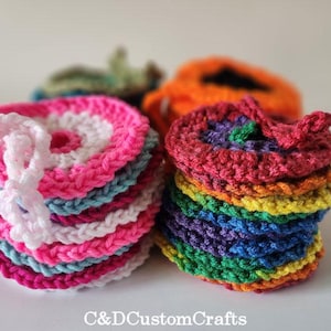 Pu&ograve; includere: Una pila di sottobicchieri all'uncinetto colorati con un design a arcobaleno. I sottobicchieri sono realizzati con filato di vari colori, tra cui rosa, blu, verde, giallo, arancione e rosso.