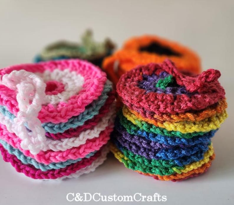 Pu&ograve; includere: Una pila di sottobicchieri all'uncinetto colorati con un design a arcobaleno. I sottobicchieri sono realizzati con filato di vari colori, tra cui rosa, blu, verde, giallo, arancione e rosso.