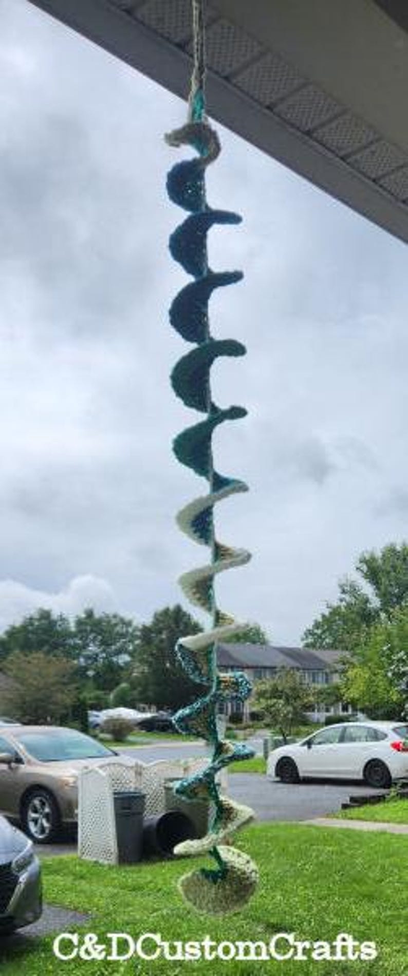 Pu&ograve; includere: Una decorazione a spirale in crochet appesa con uno schema di colori bianco e verde acqua. La decorazione &egrave; appesa a un soffitto ed &egrave; realizzata con filato.