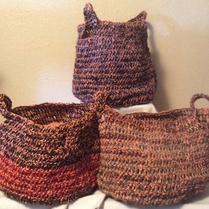 May include: Three crocheted baskets in brown, red, and blue. The baskets are made of a natural fiber and have a woven texture.