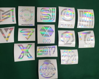 Puede incluir: Una colección de pegatinas holográficas con varios logotipos y nombres de bandas, incluyendo "EXO", "GOT7" y "TWICE". Las pegatinas se muestran sobre una superficie verde, mostrando una variedad de diseños y estilos.