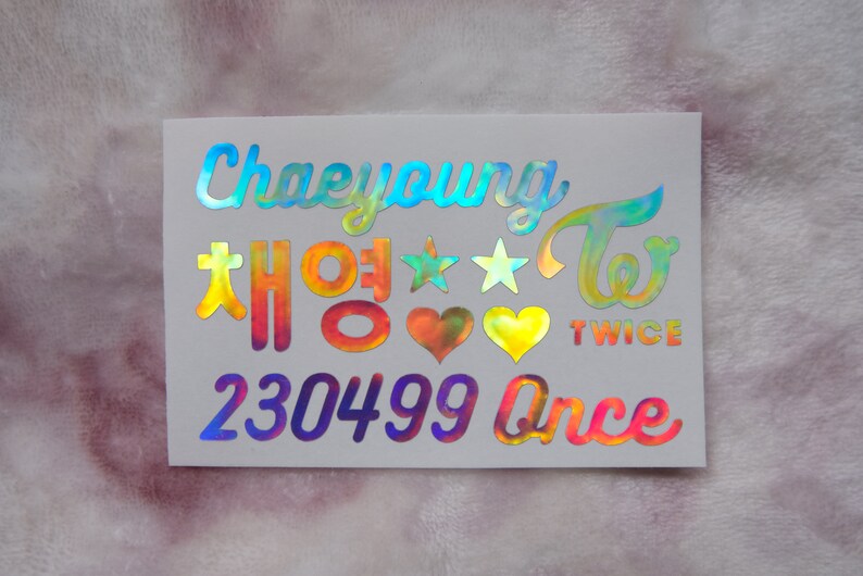 May include: Holographic sticker with the name "Chaeyoung" in a script font, along with Korean characters and the word "TWICE". Includes stars, hearts, and the word "Once". The sticker has a rainbow iridescent finish.