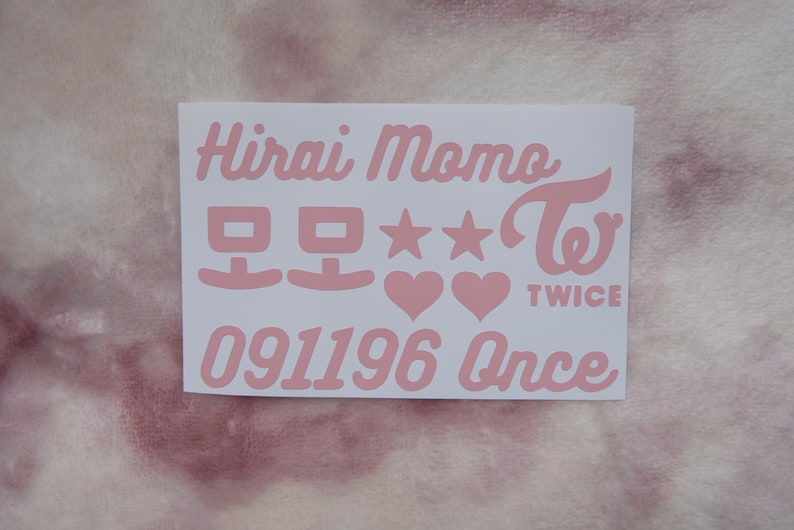 May include: A white sticker with pink text featuring the name "Hirai Momo", Korean characters, stars, hearts, the word "TWICE", the number "091196", and the word "Once". The sticker is on a pink and white background.