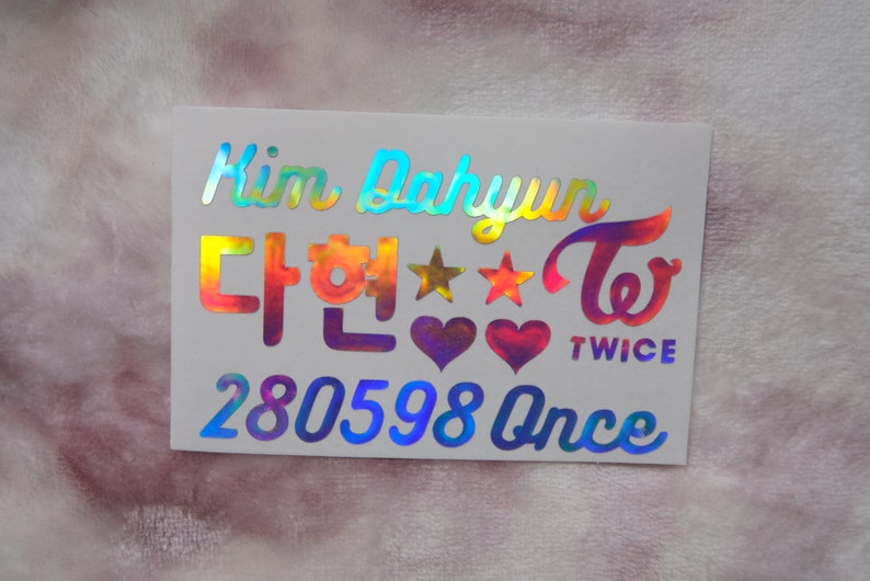 May include: A holographic sticker with the name "Kim Dahyun" and Korean characters, along with the word "TWICE" and the number "280598 Once". The sticker features stars and hearts.