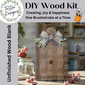 May include: A DIY wood kit with the text "DIY Wood Kit" and "Creating Joy & happiness One Brushstroke at a Time." The unfinished wood blank has a decorative border, a bow, and a button. The kit includes a jar and some fruit.