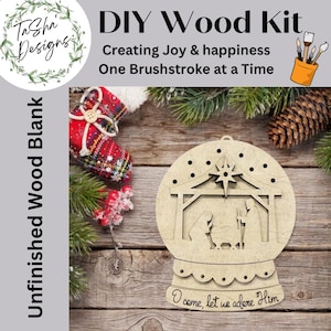 May include: DIY wood kit for a Christmas ornament. The unfinished wood blank features a snow globe design with a nativity scene, a star, and the text "O come, let us adore Him". The kit includes the text "Creating Joy & happiness One Brushstroke at a Time".