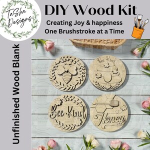 May include: DIY wood kit with four unfinished wood blanks. The blanks are round with bee and honeycomb designs, and the words "Bee Kind" and "Honey". The text "Creating Joy & happiness One Brushstroke at a Time" is also visible.