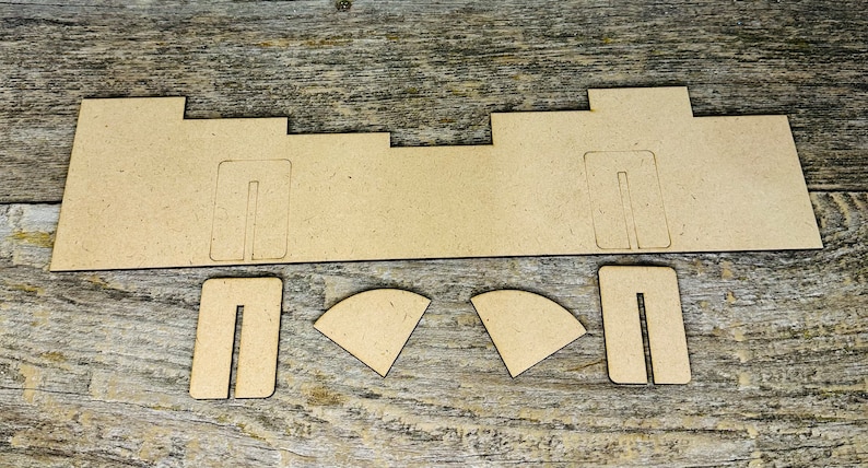 May include: A collection of unfinished, light brown wooden pieces for a craft project. The set includes a long, rectangular base with cut-out slots, two smaller rectangular pieces, and two curved pieces. The pieces are arranged on a wooden surface.