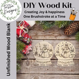 May include: DIY wood kit featuring two unfinished wood blank ornaments. Each ornament is a snow globe design with a snowman and the text "Warm Winter Wishes". The image also includes text that says "Creating Joy & happiness One Brushstroke at a Time".