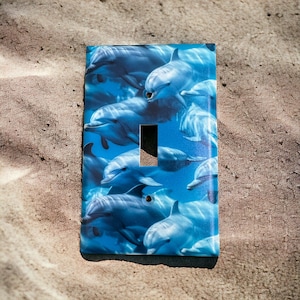 May include: A light switch cover with a blue and white image of dolphins swimming in the ocean.