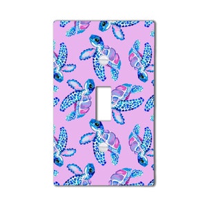 May include: A light switch cover with a pink background and a repeating pattern of blue and purple sea turtles.