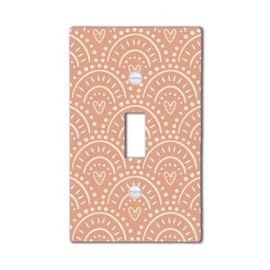 May include: A light peach-colored light switch cover with a white geometric pattern of hearts, dots, and arches.