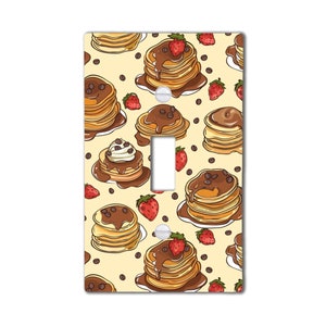 May include: A light switch cover with a pattern of pancakes, chocolate sauce, strawberries, and coffee beans. The pancakes are stacked and have a light brown color. The chocolate sauce is dark brown and drizzled over the pancakes. The strawberries are red and have green leaves. The coffee beans are brown and scattered around the pancakes.
