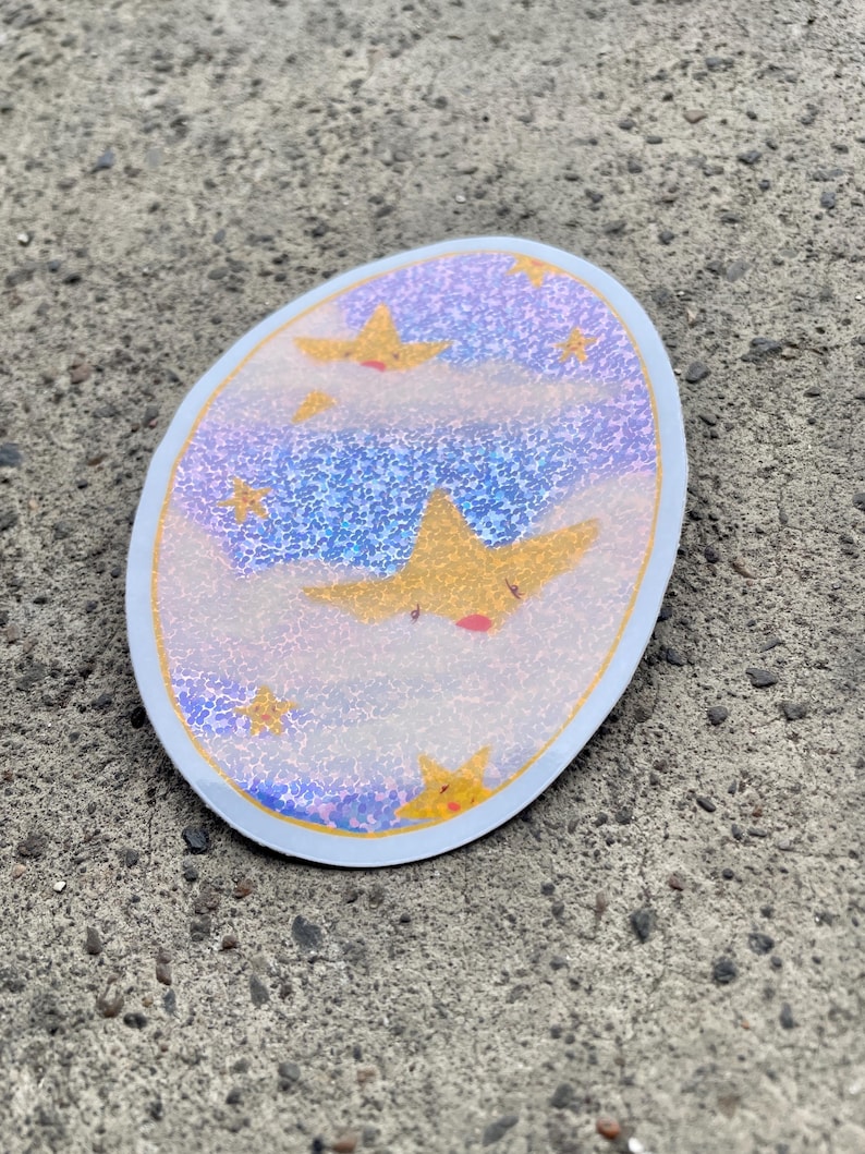 May include: A round sticker with a blue and purple glittery background with white clouds and yellow stars. The stars have a cartoon-like face with a red mouth.