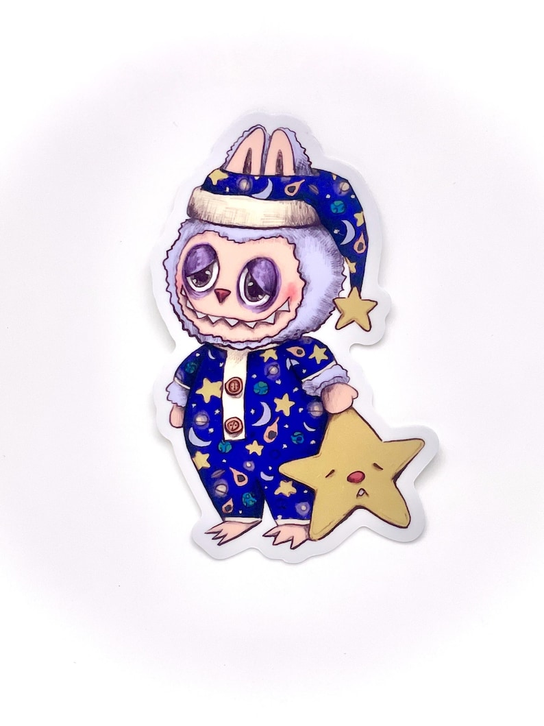 May include: A fuzzy, blue and white creature wearing a blue and white pajamas with stars, moons, and planets. The creature is holding a yellow star with a sad face.